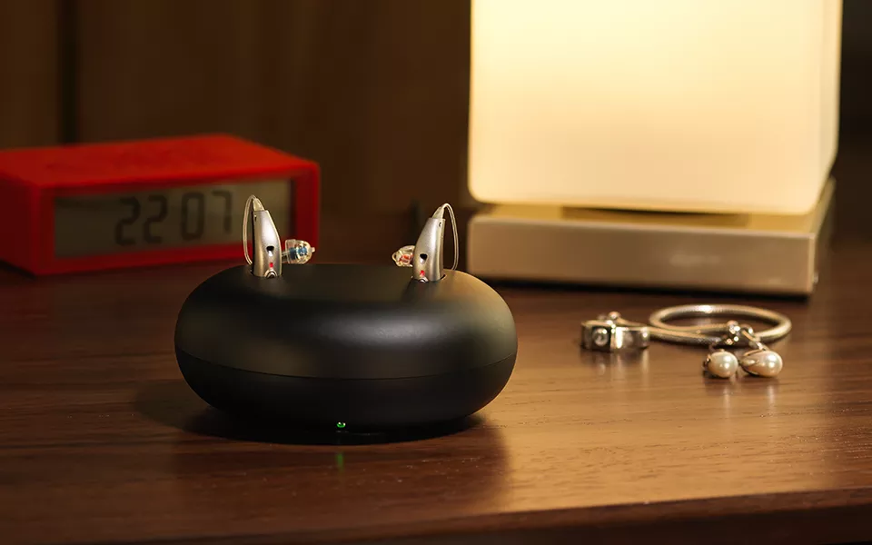 Bernafon Viron miniRITE T R lithium-ion rechargeable hearing aids in the charger on a nightable next to other personal things.